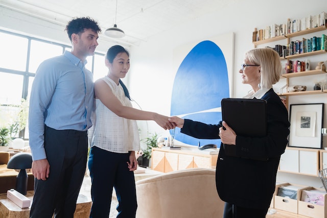 property owner holding a file and shaking hands with two prospective tenants inside a rental property