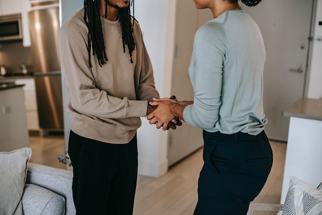 person in a tan sweater shaking hands with a person in a light blue long-sleeve shirt