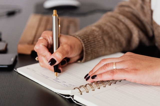 person with black nail polish writing shot list in a notebook