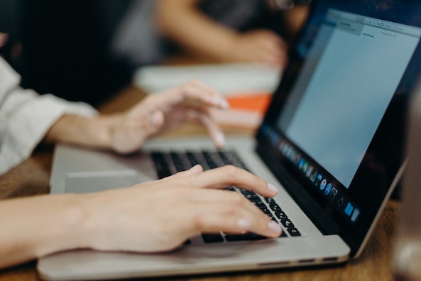 person with light pink nail polish typing on their laptop